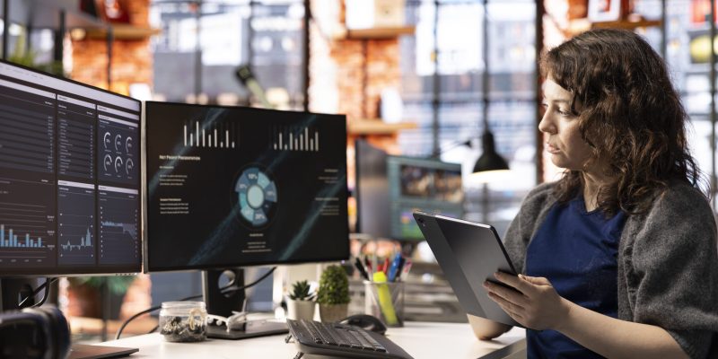 Woman at agency office using financial application UI on PC screen showing company revenue and expenses. Female expert working from apartment doing annual profits review using computer.